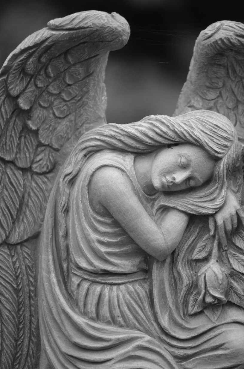 Statue of a young female angel with long hair and wings behind her as she sleeps sitting up with her head on her arm
