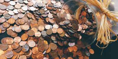 Pennies flowing from a glass carafe with a raffia ribbon bow around the neck of the carafe