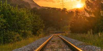 Train track with trees on either side and the sun setting in the distance.
