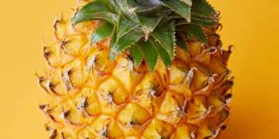 Whole fresh pineapple in front of a bold yellow background.