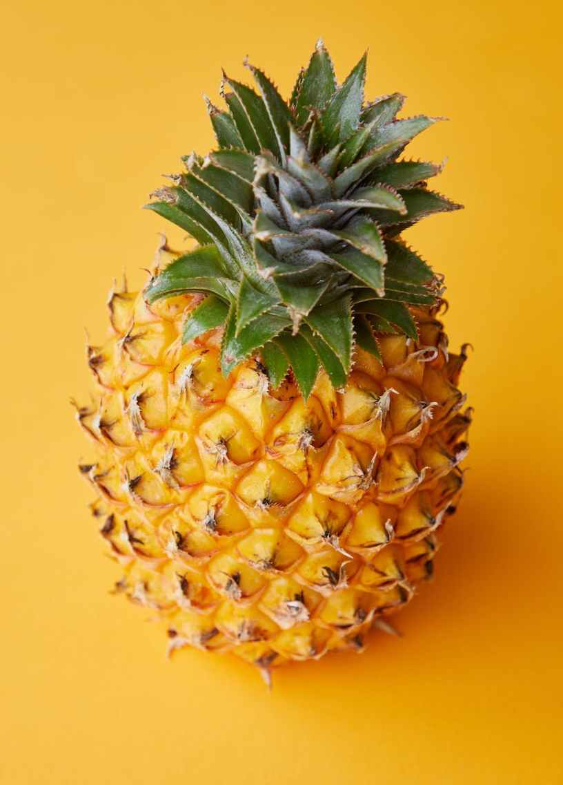 Whole fresh pineapple in front of a bold yellow background.
