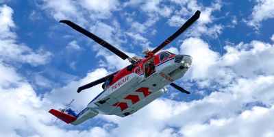 A red and white rescue helicopter flying below a cloudy blue sky.