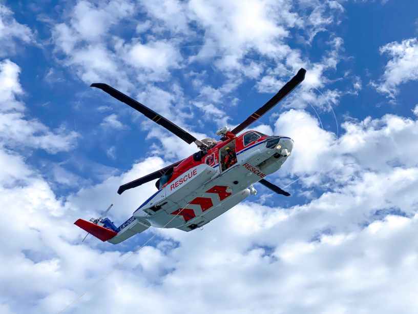 A red and white rescue helicopter flying below a cloudy blue sky.