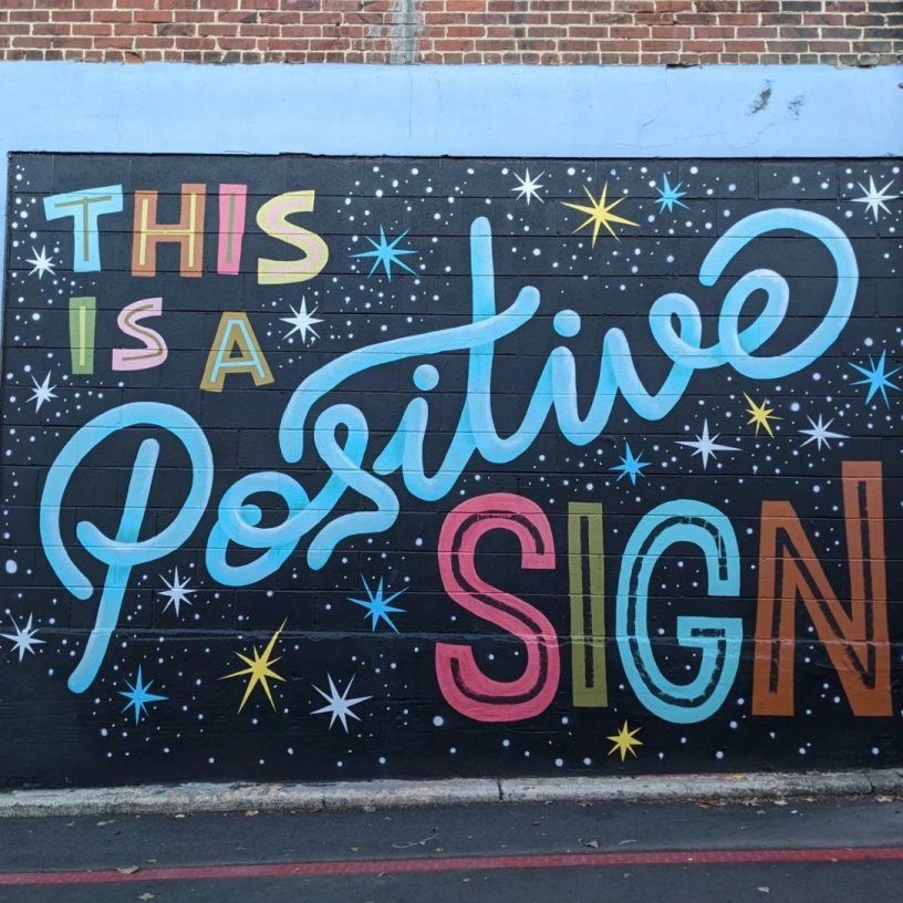 "This is a positive sign" is painted on the side of a brick building in many fun colors with star bursts.