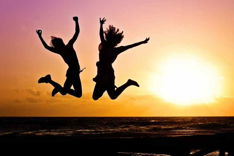 Two people jumping joyously in silhouette over the ocean with a bright sunset.