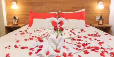 A bed with white linens covered with red rose petals.