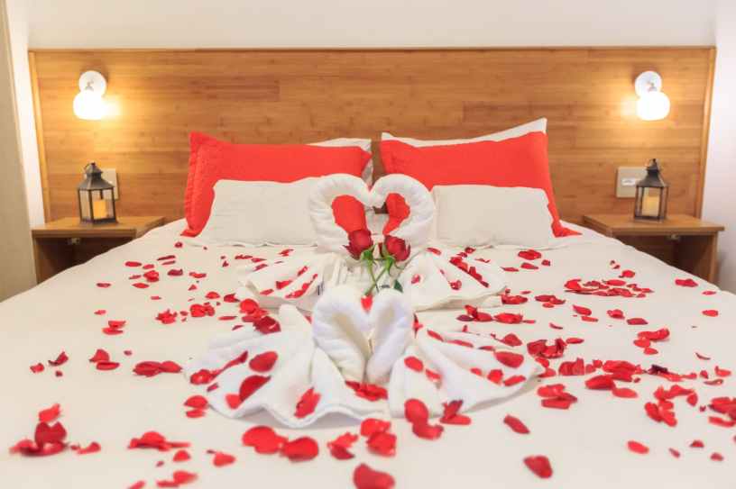 A bed with white linens covered with red rose petals.
