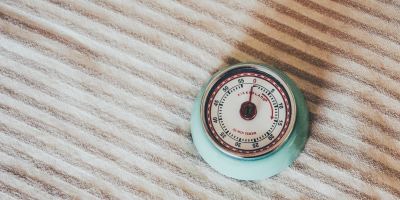 A retro kitchen timer with aqua body and red decorations on the face atop a beige striped kitchen towel.