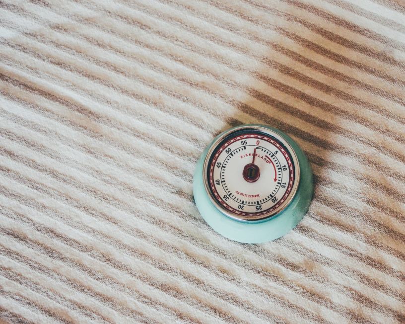 A retro kitchen timer with aqua body and red decorations on the face atop a beige striped kitchen towel.