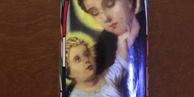 A tall glass candle with an image of baby Jesus being held by St Anthony with a woodgrain background.
