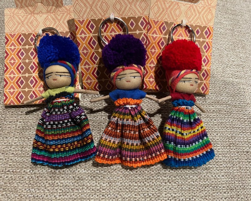 Three Guatemalan worry dolls, one with blue hair, one with purple hair and one with red hair, rest against a linen background.