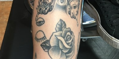 A left leg with a butterfly tattoo under the knee and below the butterfly a rose tattoo along with other tattoos.