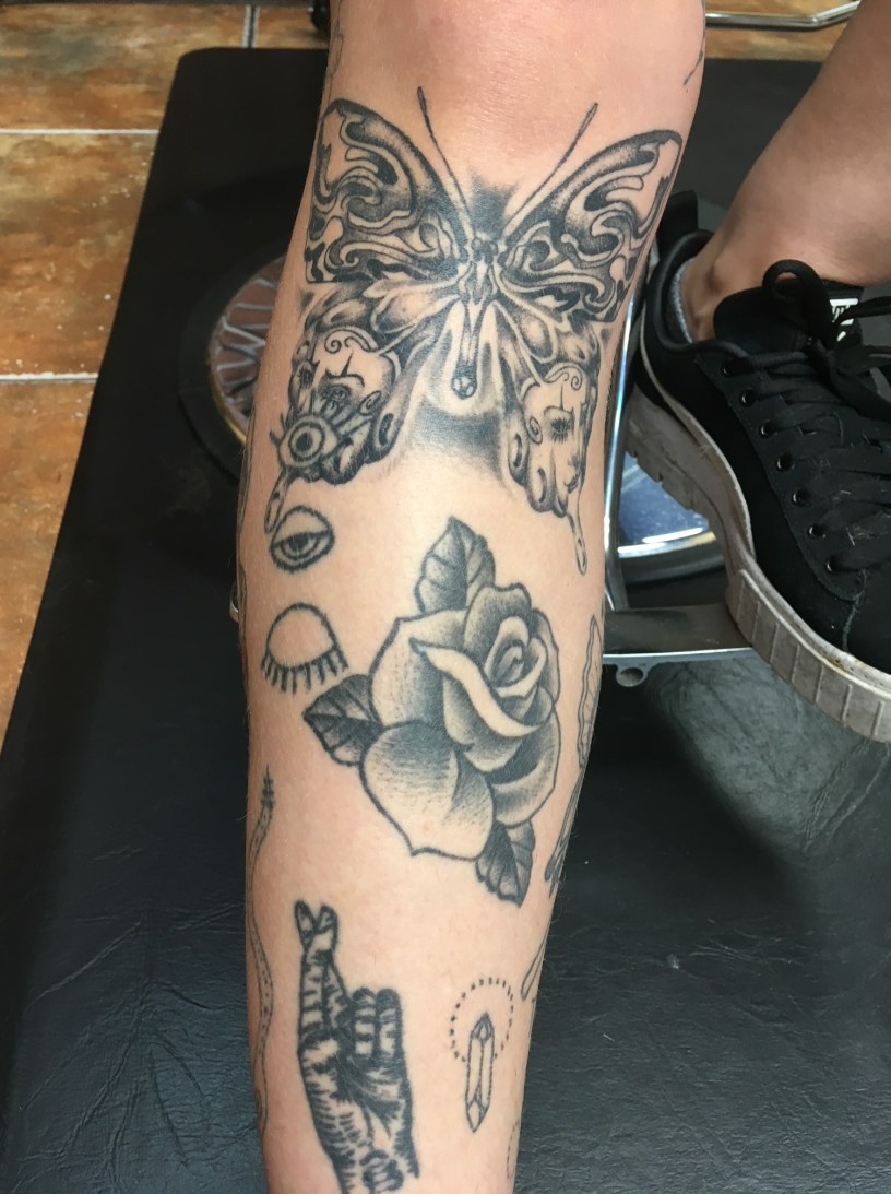 A left leg with a butterfly tattoo under the knee and below the butterfly a rose tattoo along with other tattoos.