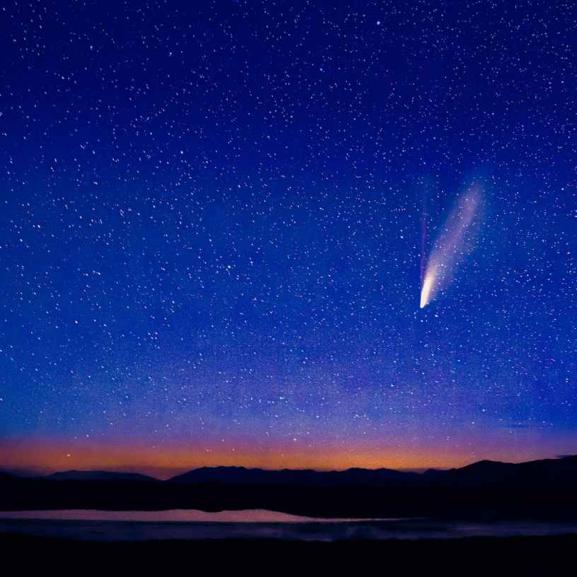 A shooting star falls through a star filled dark blue night sky.