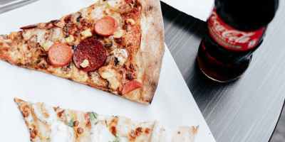 Two slices of pizza on a tray, a bottle of coke and two more slices of pizza on another tray.