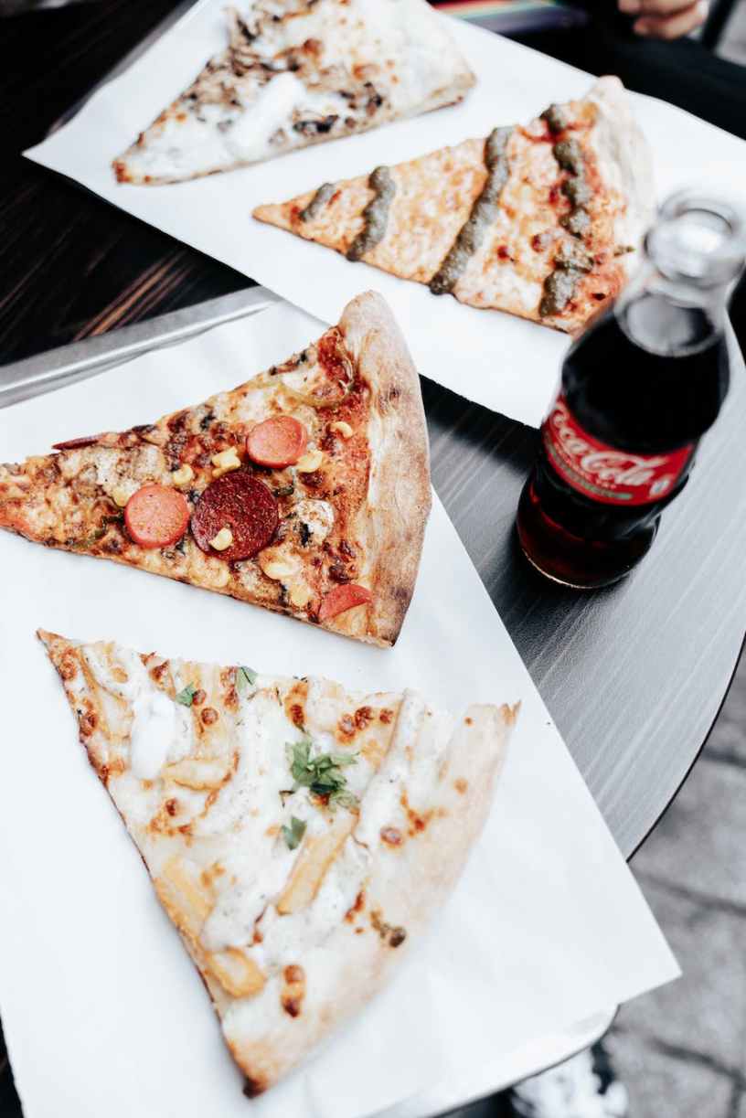 Two slices of pizza on a tray, a bottle of coke and two more slices of pizza on another tray.