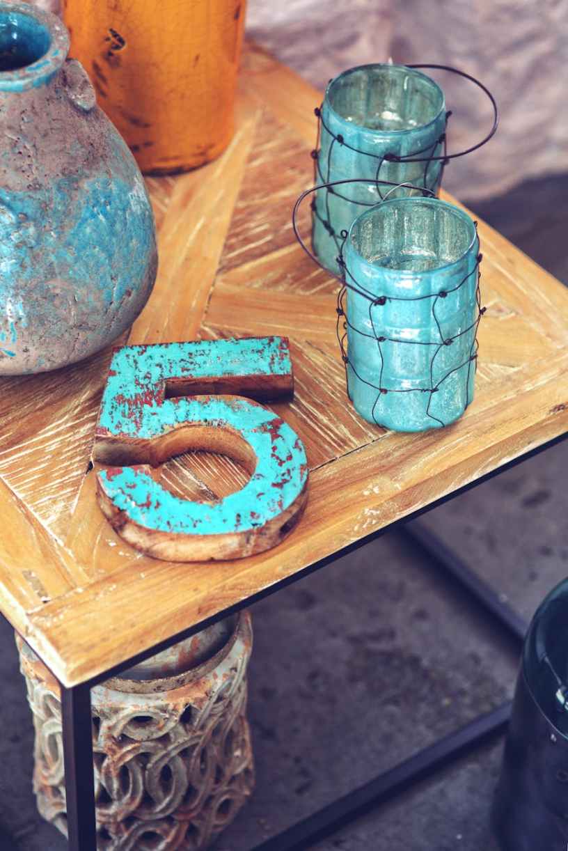 A wood table with a turquoise number 5 and a couple of candle holders and a vase.