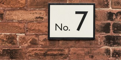 A No. 7 against a white background with a dark frame against a brick wall.