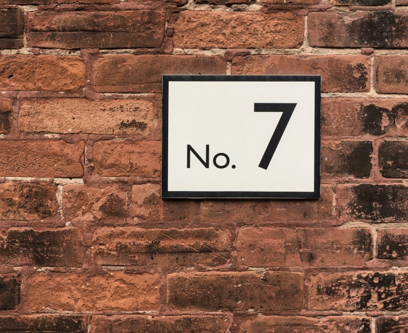 A No. 7 against a white background with a dark frame against a brick wall.
