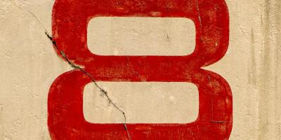A large red number eight painted on a beige wall with two cracks.