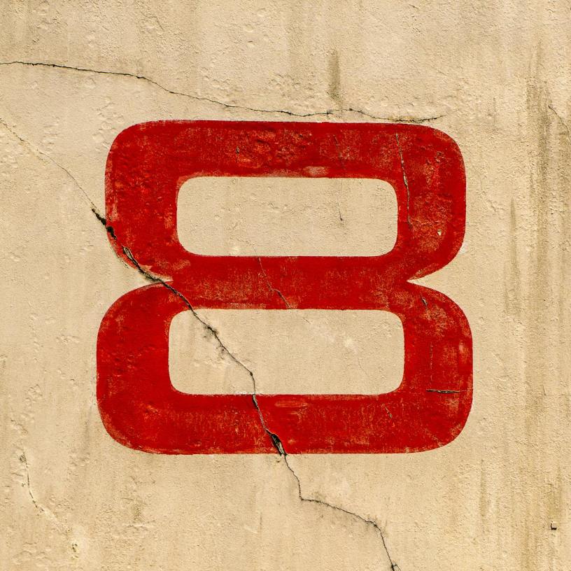 A large red number eight painted on a beige wall with two cracks.