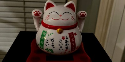 Japanese lucky cat, called Maneki Neko, is a rotund white cat with red accents and both paws raised in the air.