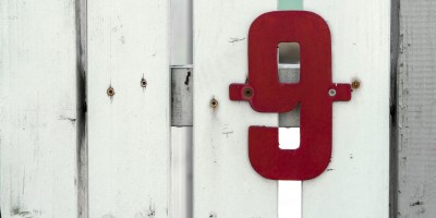 A red number nine is screwed to a white fence.