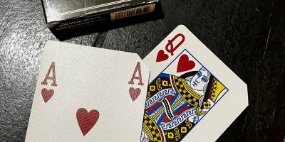 A black box that says Las Vegas Style is above two playing cards, a red ace of hearts and a red queen of hearts on a black surface.