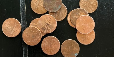 Fifteen cooper pennies, some heads up and some tails up, are scattered on a black surface.