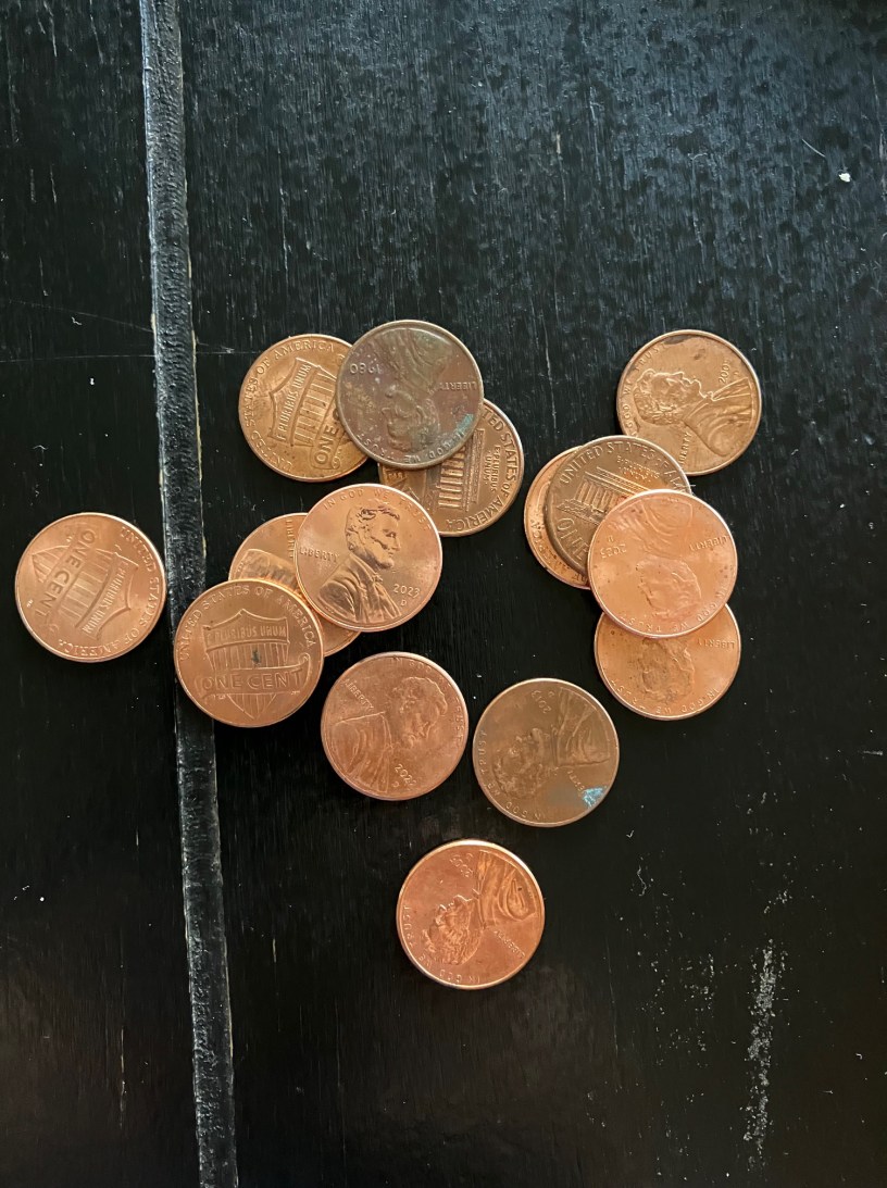 Fifteen cooper pennies, some heads up and some tails up, are scattered on a black surface.